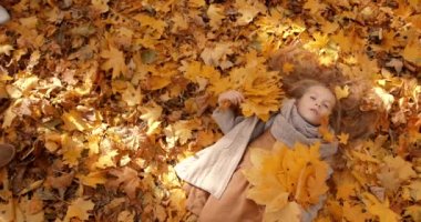 View from top to lovely blond girl lying among leaves in sunny day. Come back to school, school holidays concept.