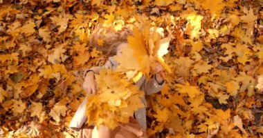 View from top to lovely blond girl lying among leaves in sunny day. Come back to school, school holidays concept.