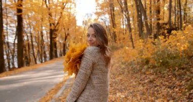Autumn sunny day. European woman standing in the yellow fall park. Holding fallen leaves and enjoying the mood.