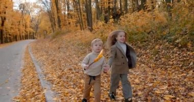 Cute little brother and sister playing on the weekend. Spending time in nature. Two schoolkids in a fall forest.
