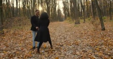Young people walking together in park in autumn. Man and woman strolling among fallen leaves in a beautiful park.