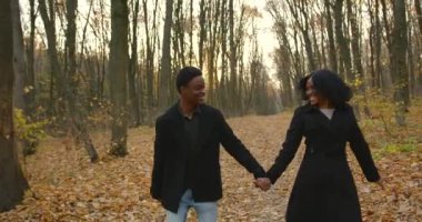 Young people walking together in park in autumn. Man and woman strolling among fallen leaves in a beautiful park.