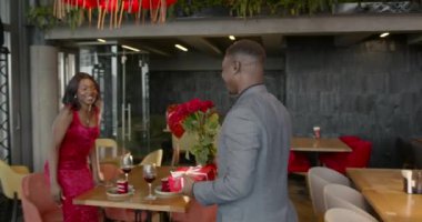 Kırmızı gülleri olan aşık bir adam restorandaki randevusuna güzel bir buket getiriyor. Kadın şaşırdı ve gülümsüyor. Çiçekler, romantik ilişki ve flört konsepti.
