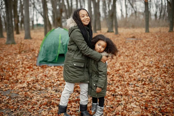 美丽的黑人小女孩站在森林的帐篷附近 两个妹妹在秋天的森林里放松 穿着卡其布外套的黑人女孩 — 图库照片