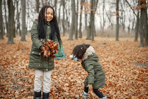 美丽的黑人小女孩站在森林的帐篷附近 两个妹妹在秋天的森林里玩黄叶 穿着卡其布外套的黑人女孩 — 图库照片