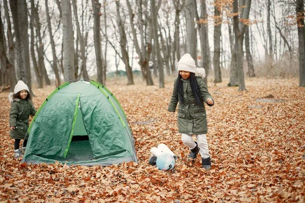 Ormanda çadırın yanında duran güzel siyah kızlar. Sonbahar ormanında oynayan iki küçük kız kardeş. Siyah kızlar haki paltolu ve bej şapkalı.