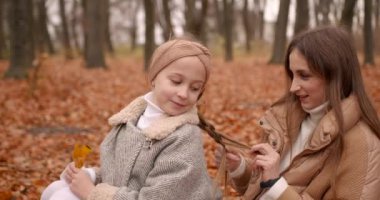 Güzel genç anne ve tatlı sarışın kızı sonbahar parkında eğleniyorlar. Anne kızına bakar, saçlarını örer..