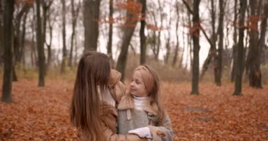 Sonbahar tatili. Küçük kız annesiyle vakit geçiriyor, düşmüş yaprakların arasında otururken sarılıyor..