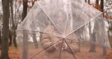 Şeffaf bir şemsiye altında kibar genç bir kadın sonbahar parkında havadan saklanır. Sonbahar mevsimi.