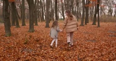 Sonbahar sezonu. Paltolu mutlu anne ve kız ormanda eğleniyor. Güzel sarı sonbahar.