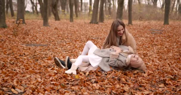 秋休み 女の子は母親と一緒に時間を過ごします 倒れた葉の間に座っている間抱擁 — ストック動画
