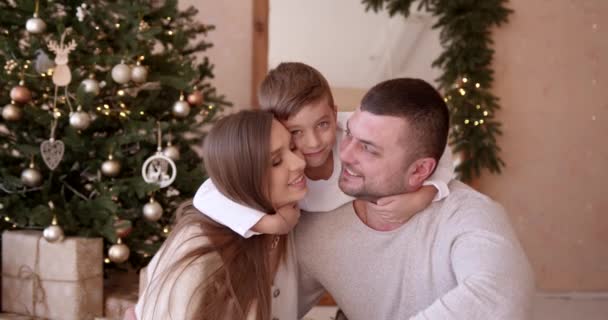 家族と一緒にクリスマスの喜び 若い両親と少年は楽しいと新年のために装飾されたインテリアで一緒に抱擁を持っています — ストック動画