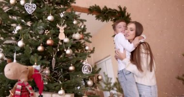 Mutlu aile yeni yıl tatiline hazırlanıyor. Sevimli oğluyla Noel ağacı süsleyen genç bir kadın. Modern konforlu evde neşeli bir atmosfer yaratmak.