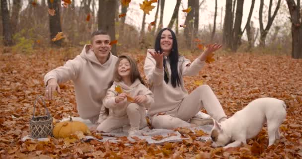 秋天令人毛骨悚然 父母和女儿在落叶丛中悠闲自在 坐在他们旁边的毛毯上 可爱的斗牛犬 — 图库视频影像
