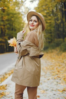 Sonbahar parkında poz veren bir kadın. Beyaz kızın dudakları kıpkırmızı. Bej ceketli ve şapkalı bir kadın..