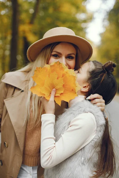 女人和她的小女孩在秋天的公园里散步 妈妈和女儿摆姿势要拍一张秋天叶子的照片 头戴米黄色外套和帽子的女人 — 图库照片