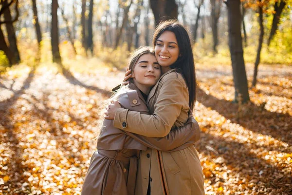 两个漂亮的女性朋友在一起 两个笑着的妹妹在秋天的公园里散步 拥抱着 穿着外套的布鲁内特和金发女孩 — 图库照片