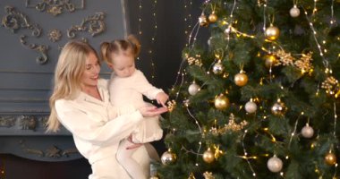 Ebeveyn ve küçük çocuk içeride noel ağacının yanında birlikte oynuyorlar. Mutlu noeller ve mutlu tatiller. Neşeli anne ve tatlı kızı.