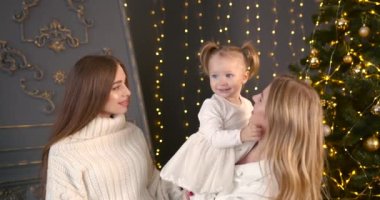 Anne ve teyze ya da iki kız kardeş küçük çocuğu öpüyor. Noel süslemeli oda. Aile kutlaması, bağlanma konsepti. Nesiller.