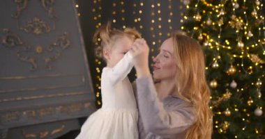 Ebeveyn ve küçük çocuk içeride noel ağacının yanında birlikte oynuyorlar. Mutlu noeller ve mutlu tatiller. Neşeli anne ve tatlı kızı.