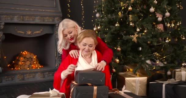 陽気な先輩女性がギフトボックスを開きます 娘と一緒に家でクリスマスを祝う — ストック動画