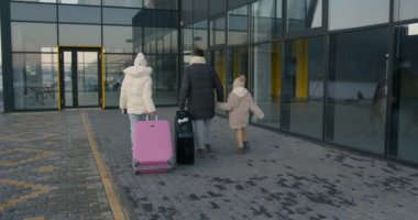Kızları havaalanı girişine doğru yürürken genç bir aile görüntüsü. Kış aile hafta sonu. Turizm konsepti