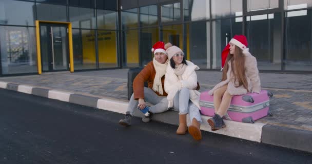Szczęśliwi Młodzi Rodzice Córką Świątecznych Kapeluszach Siedzący Walizkach Przed Lotniskiem — Wideo stockowe