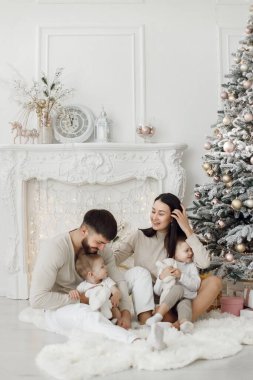 Anne, baba ve iki oğlu Noel ağacının yanında oturuyor. Heyecanlı aile Noel hediyelerini evde açıyor. Kadın, erkek ve iki çocuk beyaz elbiseli beyaz bir stüdyoda.