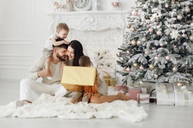 Anne, baba ve iki oğlu Noel ağacının yanında oturuyor. Heyecanlı aile Noel hediyelerini evde açıyor. Beyaz elbiseli kadın, erkek ve iki çocuk..