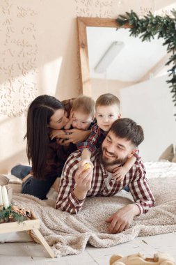 Anne, baba ve iki oğlu battaniyenin üzerinde yatıyor. Ailesi olan çocuklar birlikte vakit geçiriyorlar. Kadın, erkek ve iki çocuk ekose gömlek giyiyor..