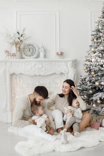 Anne, baba ve iki oğlu Noel ağacının yanında oturuyor. Heyecanlı aile Noel hediyelerini evde açıyor. Kadın, erkek ve iki çocuk beyaz elbiseli beyaz bir stüdyoda.