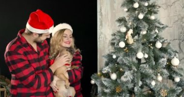 Kırmızı pijamalı bir adam ve Noel Baba şapkalı bir kadın birlikte vakit geçiriyorlar. Xmas Tree4k 'ün yanında otururken Fransız bulldogla oynarken eğleniyorum..