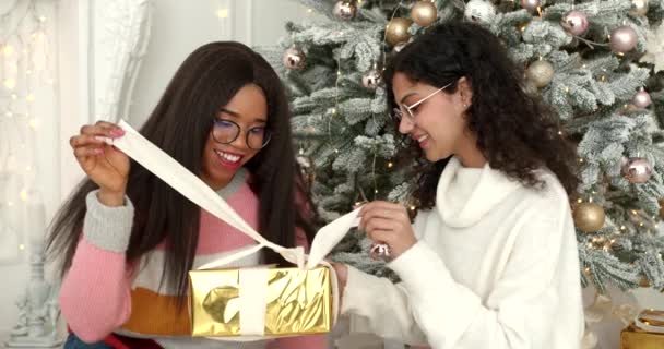 女性は家でクリスマスプレゼントを展開しています インド人と黒人の女の子お祝いの新年の休日に家 — ストック動画