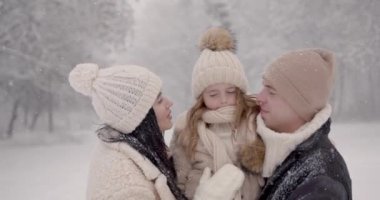 Anne ve baba, kışın doğada küçük bir çocukla karda dururlar. Tatlı kız, karlı park ayarları..