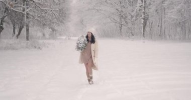 Beyaz kışlık elbiseli bir kadın Noel için hazırlanıyor. Küçük bir Noel ağacı taşıyor. Karlı orman ayarı.