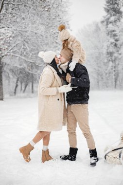 Küçük kız, baba ve anne kış günü dışarıda oynuyorlar. Esmer genç bir kadın, kışın sıcak ceketli bir adam ve küçük bir kız kızakla parkta yürüyorlar. Anne ve kızı kışı giyiyor.