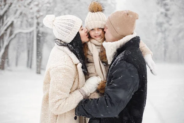 冬の日に屋外で遊んでいる少女 父と母 暖かいジャケットで冬のブルネットの若い女性 男と女の子は公園を歩いて抱擁します 冬を着た母と娘 — ストック写真