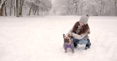 Şapkalı ve eldivenli şirin küçük kız karlı bir parkta köpekle oynuyor. Aktif hafta sonu açık hava