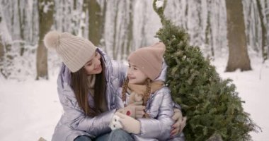 Genç bir kadın ve küçük kızı karlı bir ormanda birlikte vakit geçiriyorlar. Noel hediyeleriyle bir köknar ağacının yanında oturuyorlar. Noel tatili kavramı.