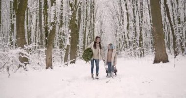 Kızıyla birlikte kızak taşıyan genç bir kadın. Noel kutuları ve köknar ağacı. Tatiller.