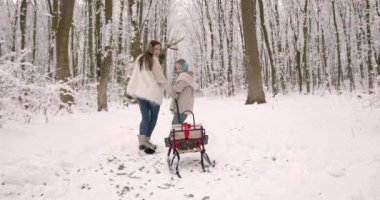 Kızıyla birlikte kızak taşıyan genç bir kadın. Noel kutuları ve köknar ağacı. Tatiller.