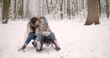 Parkta aile kış eğlencesi. Anne ve kızı kışın karda dışarıda eğleniyorlar..