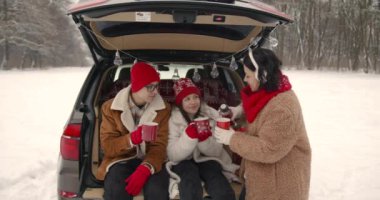 Anne ve iki çocuk hafta sonu dışarıda eğleniyor. Bir arabanın bagajında oturup fincanlardan, Noel atmosferinden çay içiyorlar..