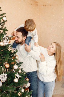 Bir anne ve baba ve oğulları Noel ağacını oyuncaklarla süslüyorlar. Oğlu babasının omuzlarında oturuyor. Anne, baba ve küçük çocuk beyaz süveter giyiyor..