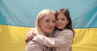 Ukrayna 'nın mavi ve sarı bayrağının yanında gülümseyen ve kucaklaşan kadın ve kızı. Aile, birlik, destek. Ukraynalılar savaşa karşıdır. Kadın ve çocuk.