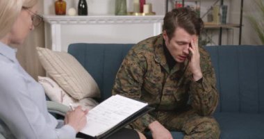 Askeri üniformalı sıkıntılı genç adam terapi sırasında psikologla konuşuyor, içeride. Yardım, destek, travma sonrası stres bozukluğu, sağlık ve uyum kavramı.