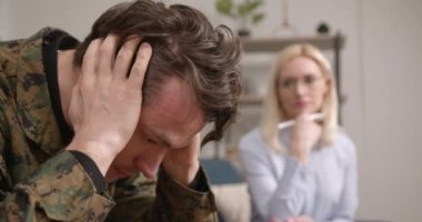 Askeri üniformalı sıkıntılı genç adam terapi sırasında psikologla konuşuyor, içeride. Yardım, destek, travma sonrası stres bozukluğu, sağlık ve uyum kavramı.