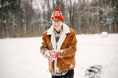 Çocuk kış parkında vakit geçiriyor. Kar yağdıran bir genç. Sıkı bir ceket ve örgü şapka giyen bir çocuk..