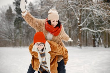 Oğlu annesini sırtında taşıyor. Neşeli çocuk ve güzel annesi kış parkında birlikte vakit geçiriyorlar. Sıcak ceket ve kırmızı kazak giyen bir kadın..