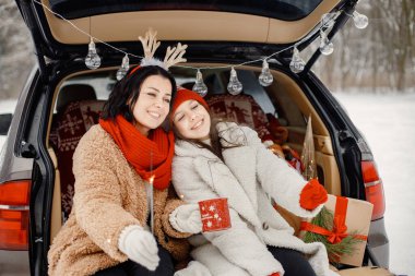 Anne ve genç kızı kış parkında birlikte vakit geçiriyorlar. Aile açık arabaların bagajında oturuyor ve ellerinde çay ve maytapla kırmızı bardaklar tutuyor. Aile kalın ceketler ve örgü şapkalar giyiyor..